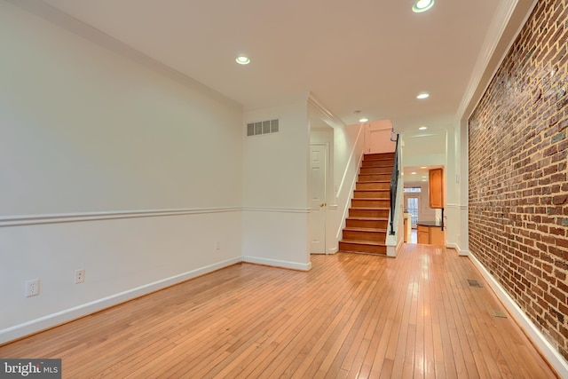 interior space with light wood finished floors, visible vents, brick wall, baseboards, and stairs