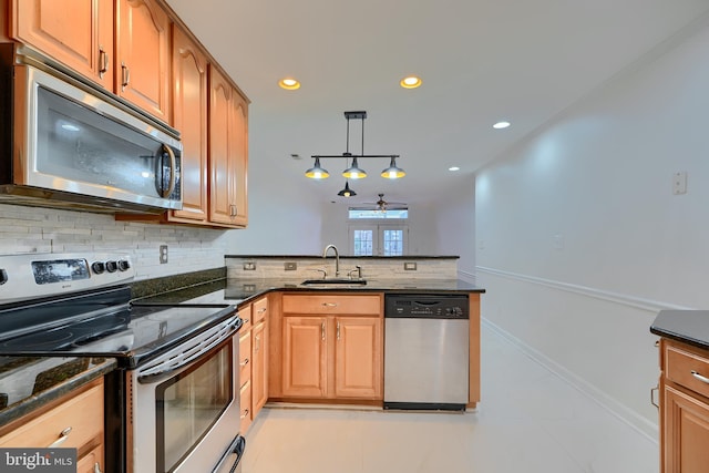 kitchen featuring a sink, tasteful backsplash, stainless steel appliances, dark stone counters, and a peninsula