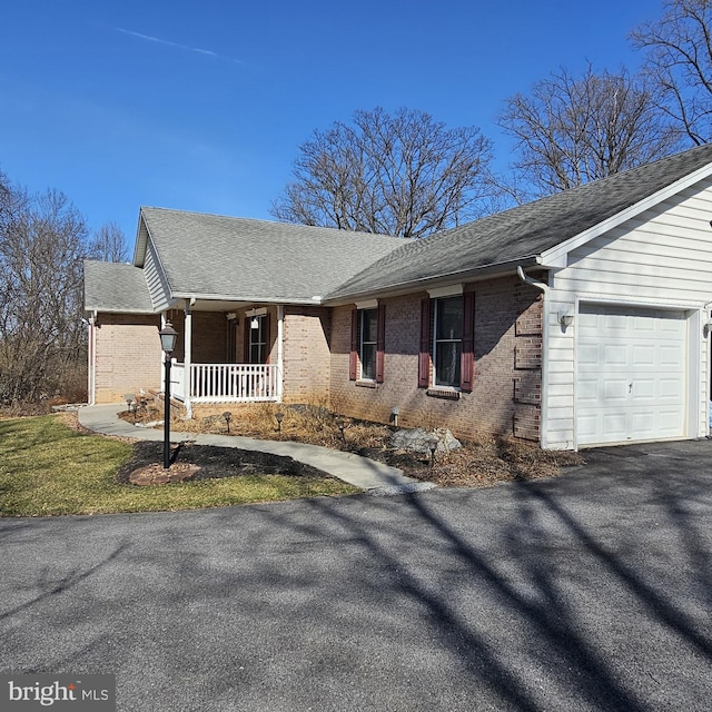 view of front facade featuring covered porch, a shingled roof, a garage, aphalt driveway, and brick siding