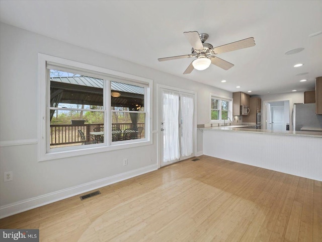 unfurnished living room with light wood finished floors, visible vents, baseboards, and ceiling fan