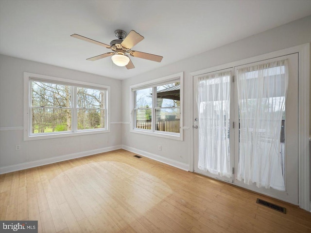 spare room featuring wood finished floors, baseboards, a ceiling fan, and visible vents
