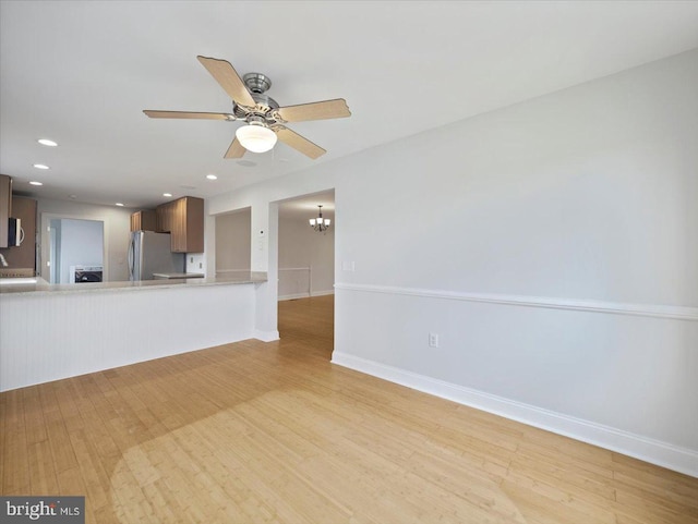 unfurnished living room featuring baseboards, light wood-type flooring, recessed lighting, and ceiling fan with notable chandelier