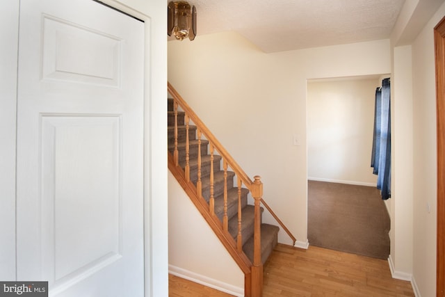 staircase with a textured ceiling, baseboards, and wood finished floors