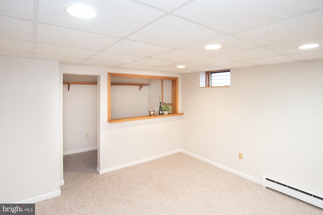 basement featuring a paneled ceiling, carpet, baseboards, and a baseboard radiator