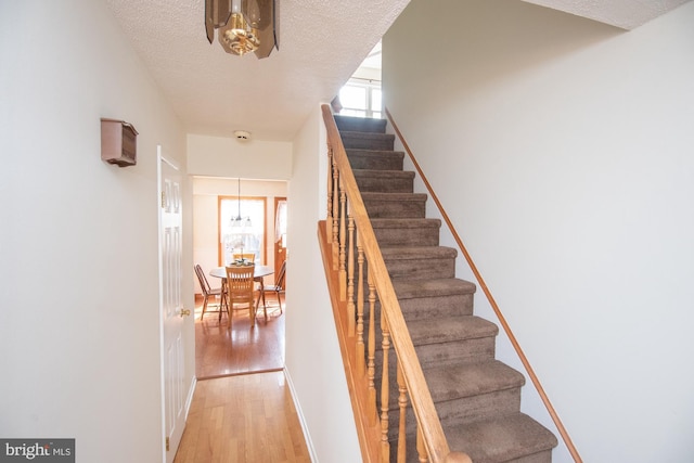 stairway with baseboards, a textured ceiling, and wood finished floors