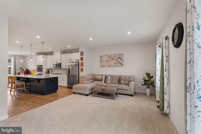 living area featuring recessed lighting, light colored carpet, baseboards, and light wood-type flooring