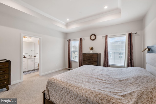 bedroom featuring a sink, a tray ceiling, ensuite bath, baseboards, and light colored carpet