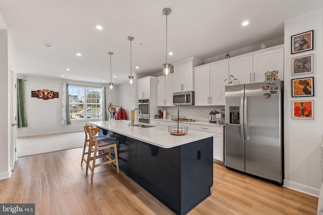 kitchen with tasteful backsplash, an island with sink, stainless steel appliances, white cabinetry, and a sink