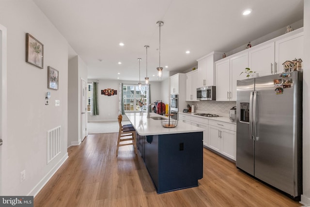 kitchen with visible vents, a center island with sink, appliances with stainless steel finishes, white cabinetry, and a sink