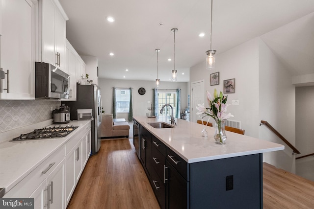 kitchen with a center island with sink, a sink, white cabinetry, appliances with stainless steel finishes, and light countertops