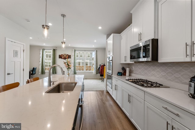 kitchen with wood finished floors, a sink, decorative backsplash, white cabinets, and appliances with stainless steel finishes