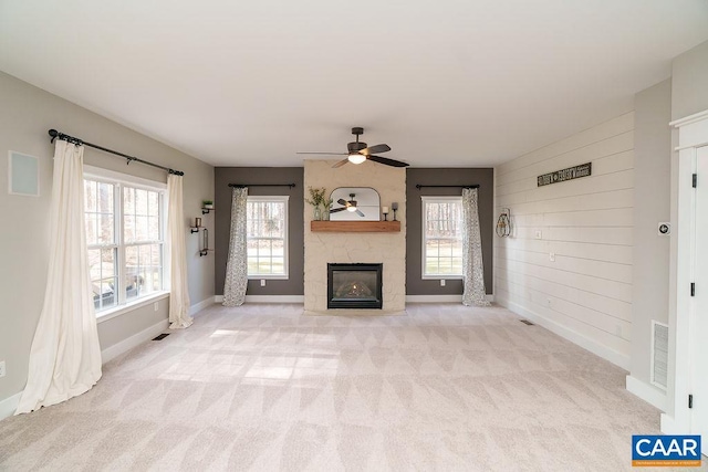 unfurnished living room featuring visible vents, plenty of natural light, carpet, and a stone fireplace