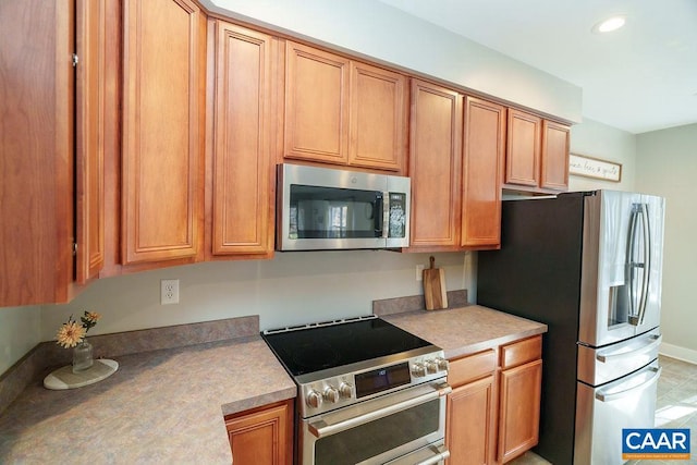 kitchen featuring recessed lighting, appliances with stainless steel finishes, brown cabinetry, light countertops, and baseboards