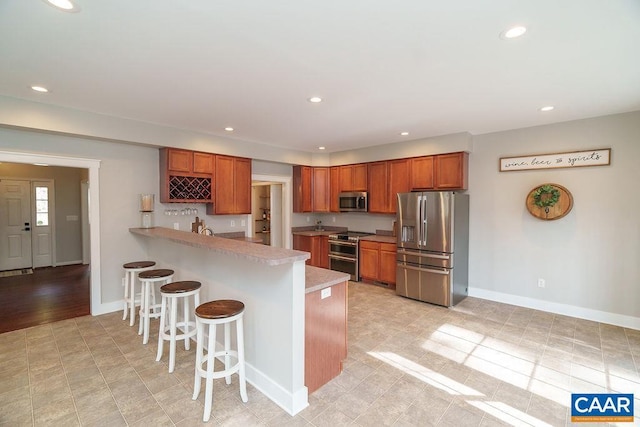 kitchen featuring a breakfast bar area, light countertops, a peninsula, brown cabinetry, and stainless steel appliances