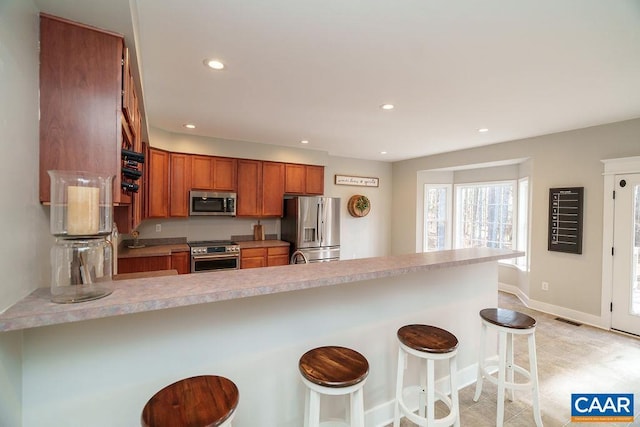 kitchen with visible vents, brown cabinets, appliances with stainless steel finishes, a kitchen breakfast bar, and a peninsula