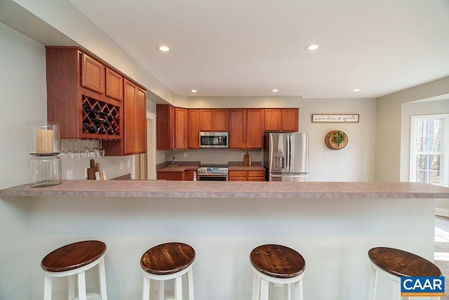 kitchen with brown cabinetry, a peninsula, recessed lighting, light countertops, and appliances with stainless steel finishes