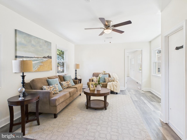 living area with visible vents, light wood-style flooring, a ceiling fan, and baseboards