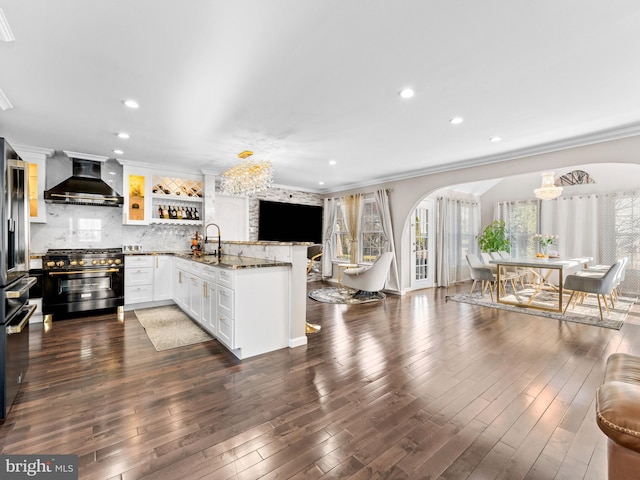 kitchen with a sink, arched walkways, a peninsula, wall chimney exhaust hood, and high end range