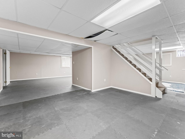 basement with stairway, a paneled ceiling, and baseboards