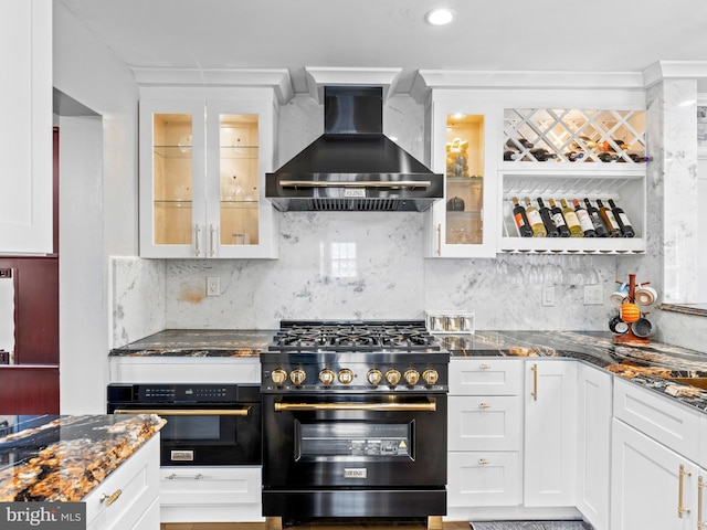 kitchen featuring oven, wall chimney exhaust hood, stainless steel stove, and dark stone countertops