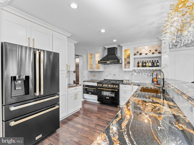 kitchen with stainless steel refrigerator with ice dispenser, a sink, high end black range, white cabinetry, and wall chimney exhaust hood