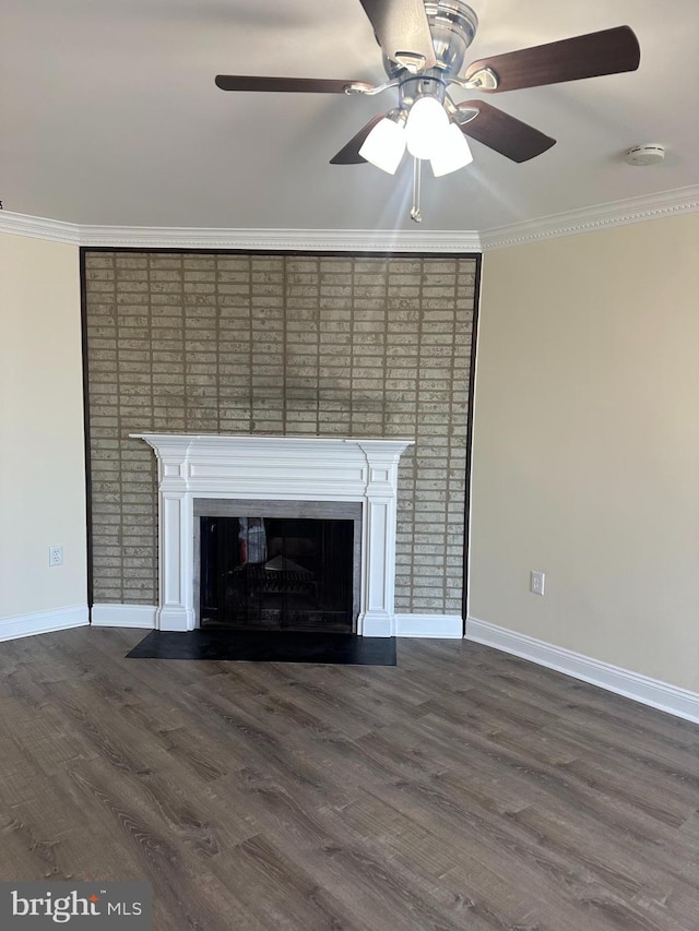 unfurnished living room with ornamental molding, a glass covered fireplace, dark wood-style floors, baseboards, and ceiling fan