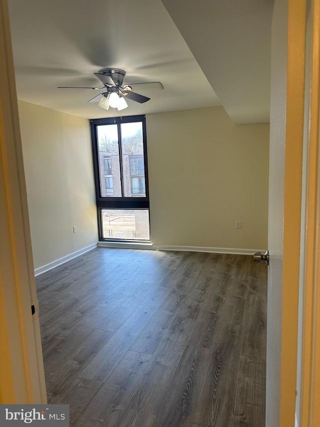 unfurnished room featuring dark wood finished floors, a ceiling fan, and baseboards