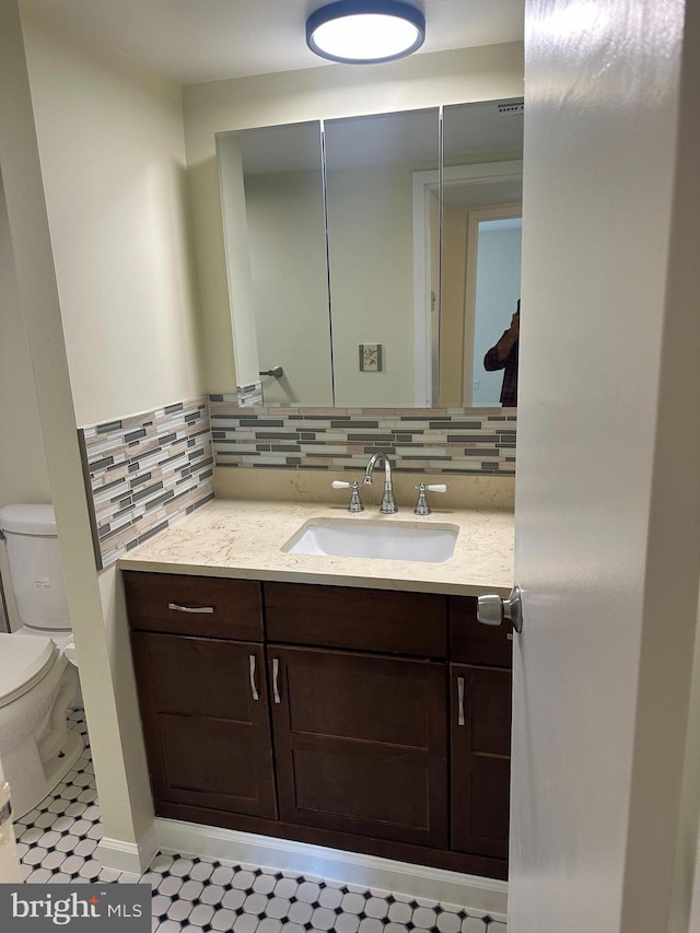 half bath featuring tile patterned floors, backsplash, toilet, and vanity