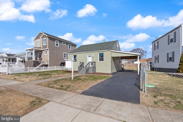 view of front of house featuring fence, aphalt driveway, a residential view, roof with shingles, and a carport