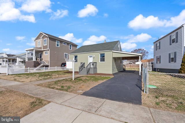 view of front of house featuring fence, aphalt driveway, a residential view, roof with shingles, and a carport