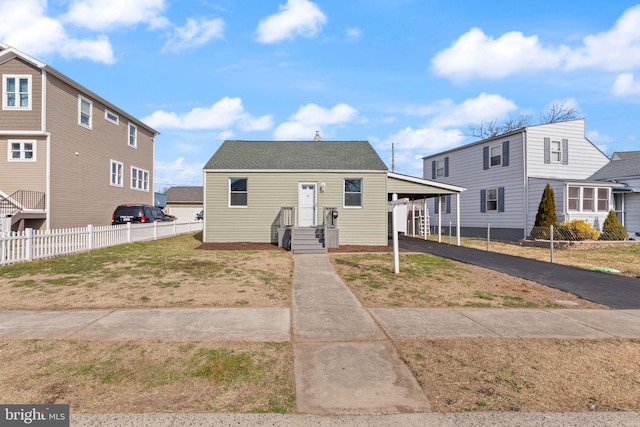 view of front of home with aphalt driveway, roof with shingles, a carport, and fence