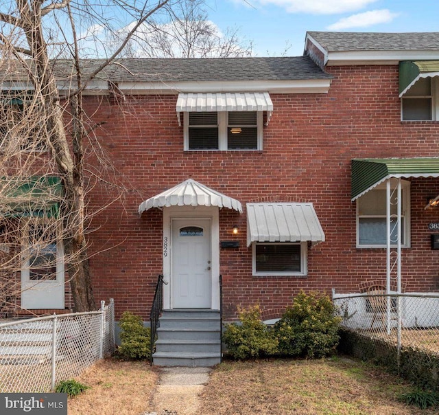 view of front of home featuring brick siding, roof with shingles, entry steps, and fence