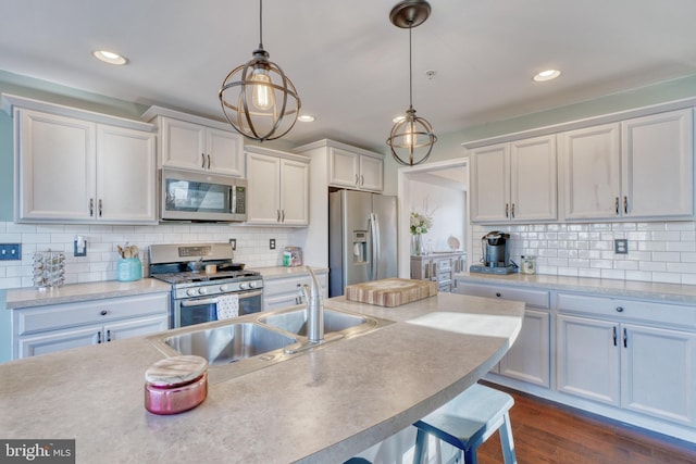 kitchen featuring dark wood-style flooring, a sink, hanging light fixtures, appliances with stainless steel finishes, and backsplash