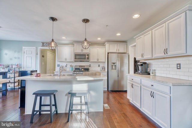 kitchen featuring a breakfast bar, dark wood finished floors, a sink, stainless steel appliances, and white cabinets