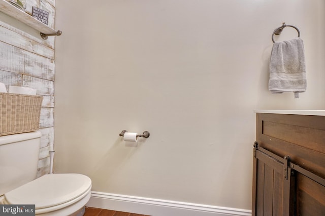 half bath with vanity, toilet, wood finished floors, and baseboards