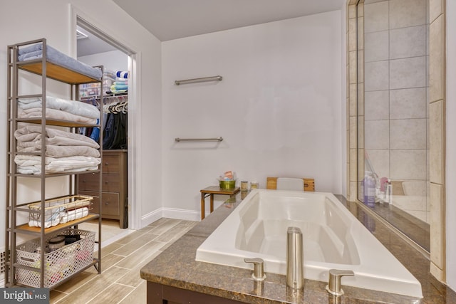 bathroom with a bath, a walk in closet, baseboards, and wood tiled floor