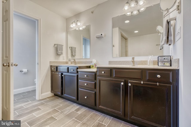 full bathroom with baseboards, wood tiled floor, toilet, double vanity, and a sink