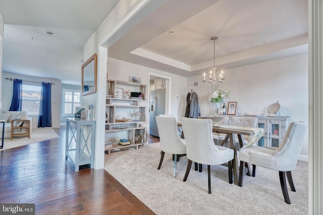 dining area featuring baseboards, visible vents, dark wood finished floors, an inviting chandelier, and a raised ceiling