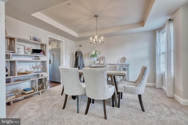 carpeted dining area with a tray ceiling, visible vents, baseboards, and a chandelier