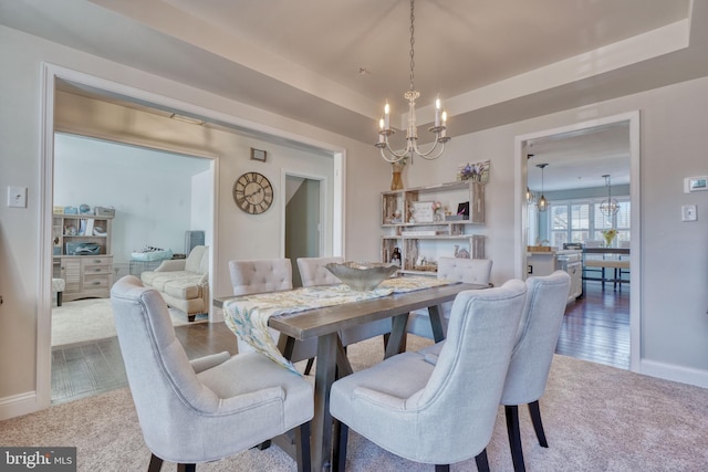 dining room featuring wood finished floors, baseboards, carpet floors, a raised ceiling, and a notable chandelier