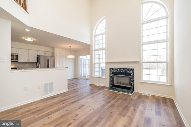 unfurnished living room featuring visible vents, baseboards, a high ceiling, light wood-style flooring, and a high end fireplace