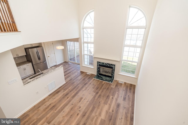 unfurnished living room featuring visible vents, light wood-style flooring, a fireplace, a high ceiling, and a sink