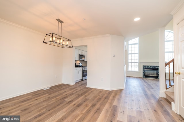 unfurnished dining area featuring baseboards, light wood-type flooring, a premium fireplace, ornamental molding, and an inviting chandelier