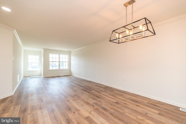 unfurnished room with a notable chandelier, ornamental molding, baseboards, and wood finished floors