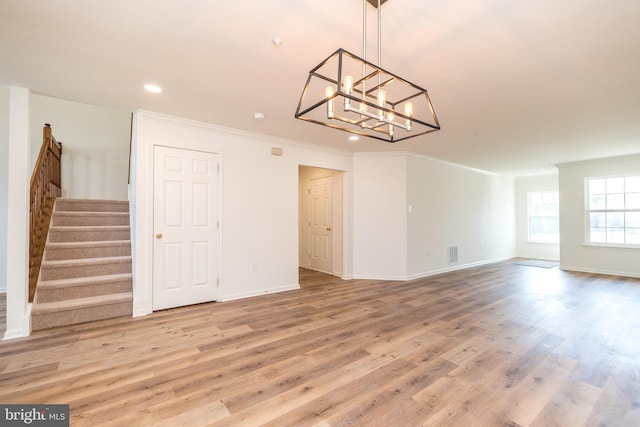 unfurnished living room featuring light wood-type flooring, a notable chandelier, crown molding, baseboards, and stairs