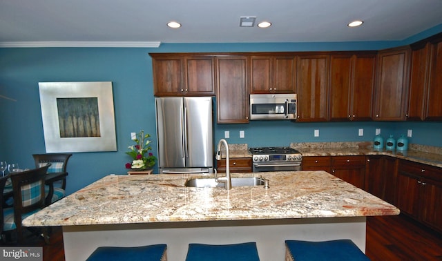 kitchen featuring light stone counters, recessed lighting, a sink, appliances with stainless steel finishes, and a kitchen breakfast bar