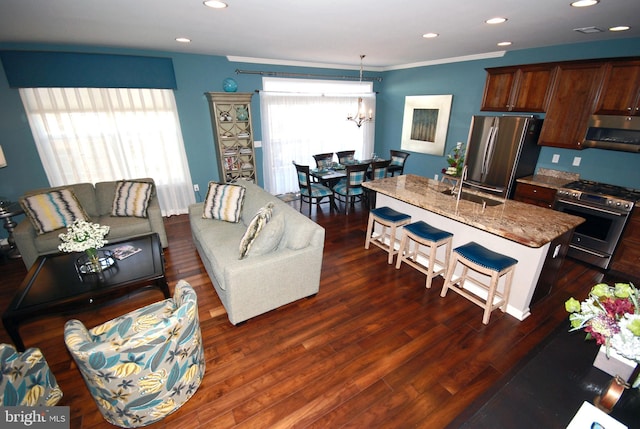 interior space with a kitchen bar, a center island with sink, a sink, dark wood-style floors, and appliances with stainless steel finishes