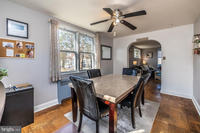 dining space featuring baseboards, arched walkways, radiator, and a ceiling fan