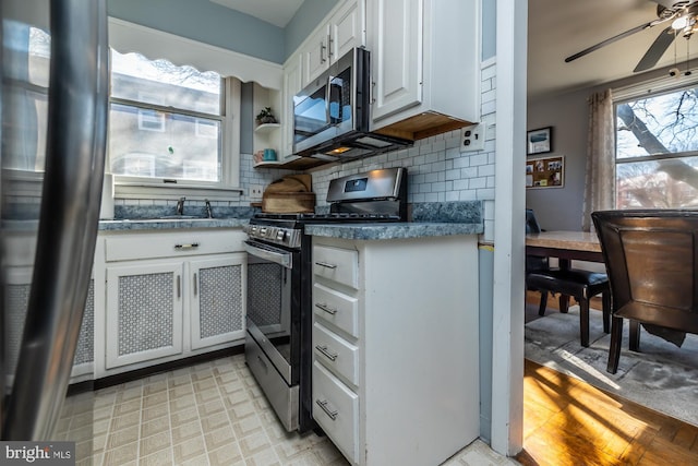 kitchen featuring tasteful backsplash, white cabinetry, appliances with stainless steel finishes, light floors, and ceiling fan