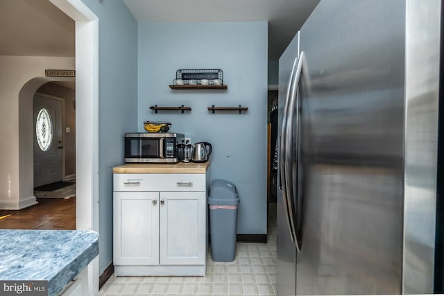 kitchen featuring stainless steel appliances, arched walkways, baseboards, and white cabinets